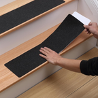 Person installing black stair treads on wooden stairs