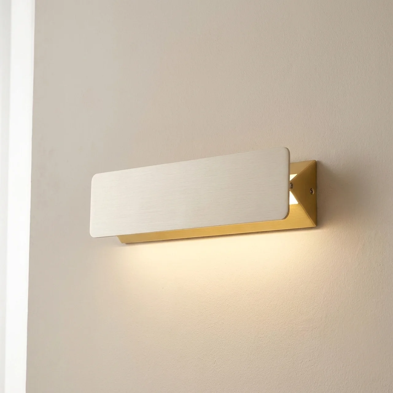 Modern wall light fixture with gold frame and white glass on a neutral wall.