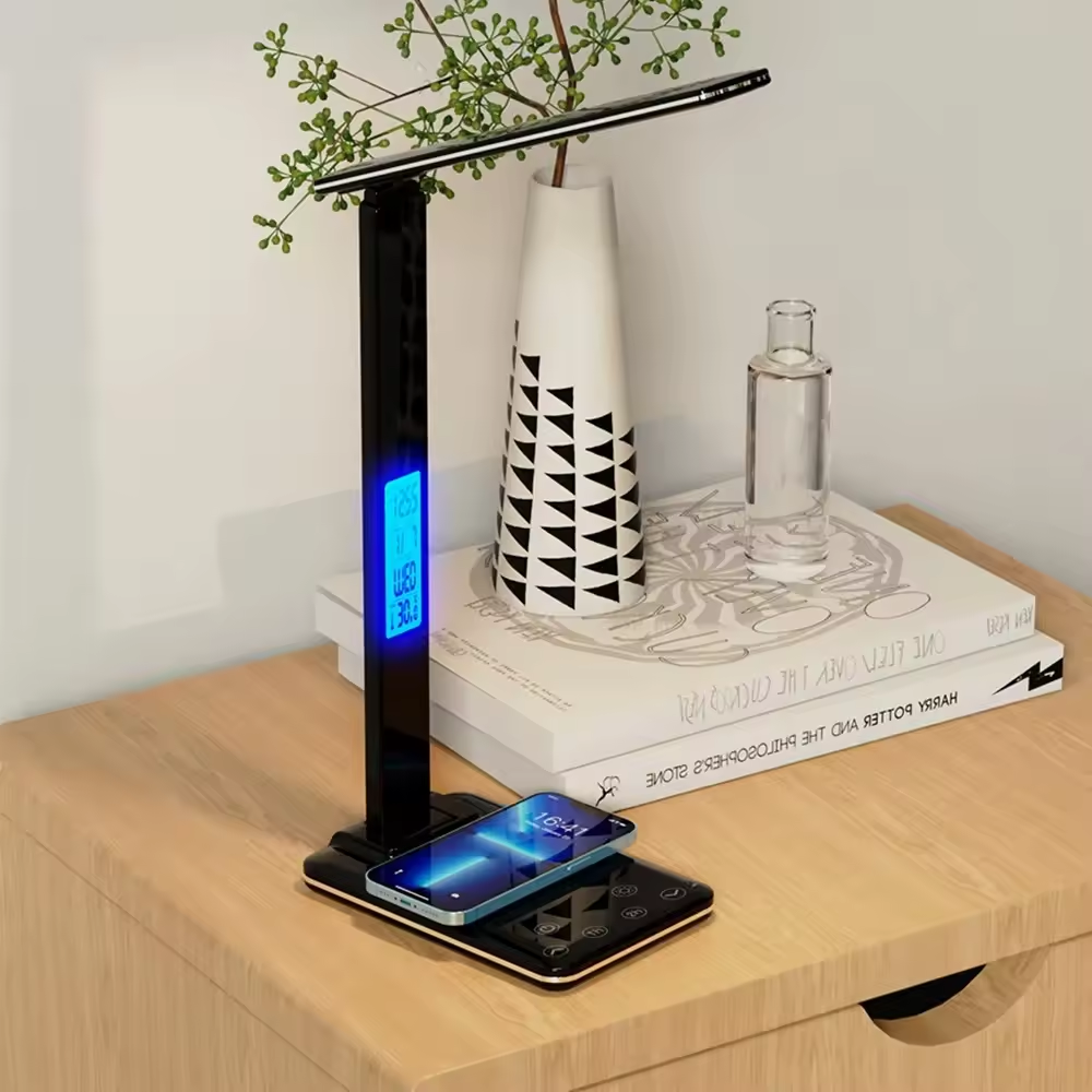 Black LED desk lamp with phone charging station on a wooden surface.