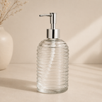 Clear glass soap dispenser with silver pump on a beige background