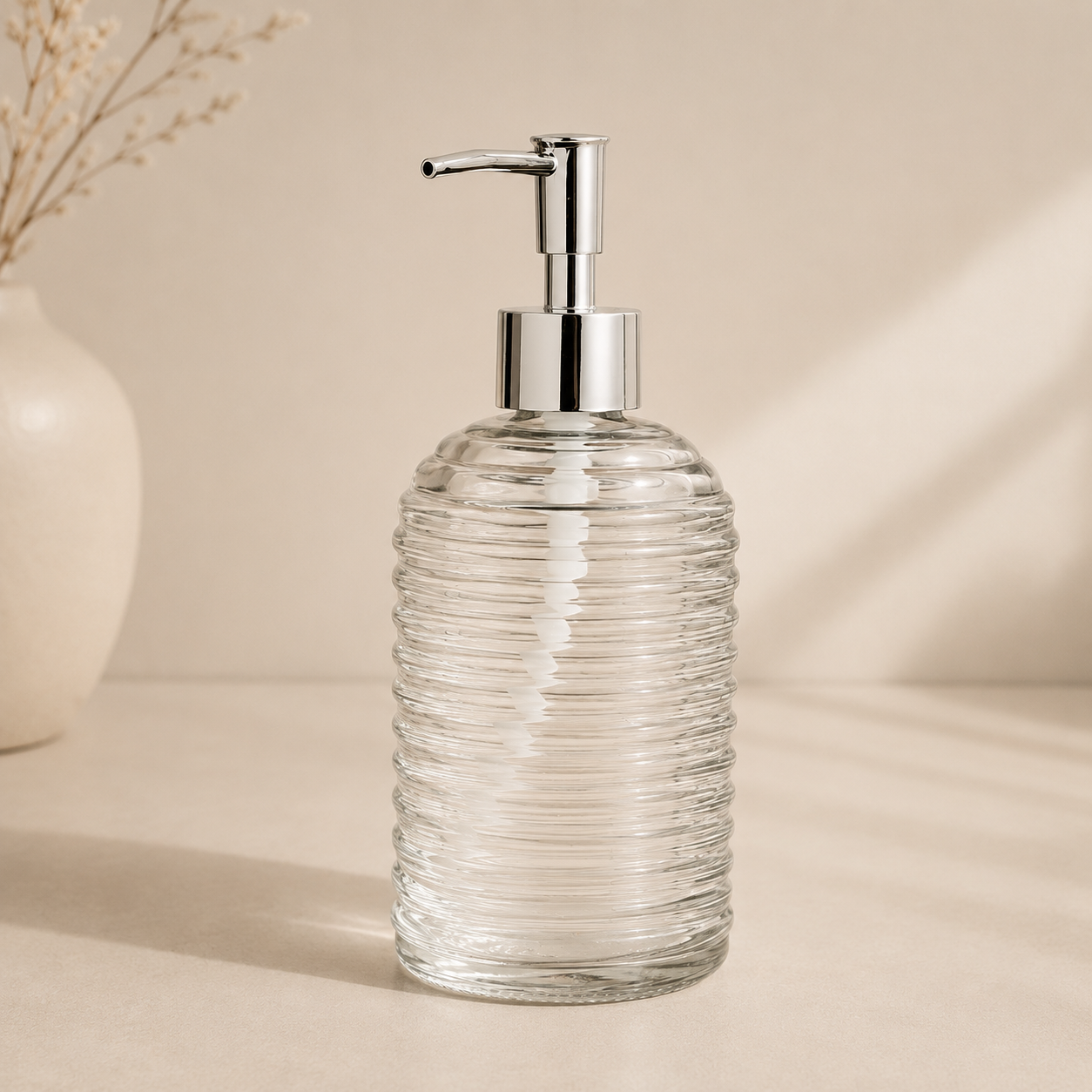 Clear glass soap dispenser with silver pump on a beige background