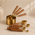 Set of brass measuring cups and spoons with wooden handles on a beige surface.