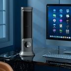 Gray tower fan on a desk next to a computer monitor with a blue wall background