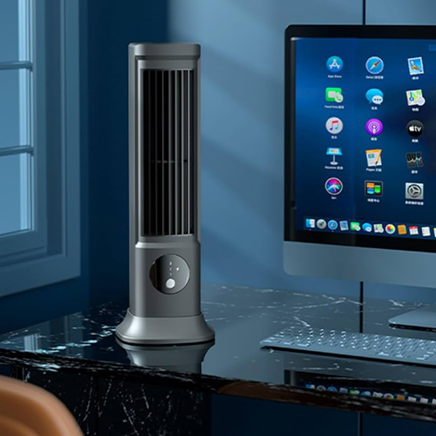 Gray tower fan on a desk next to a computer monitor with a blue wall background