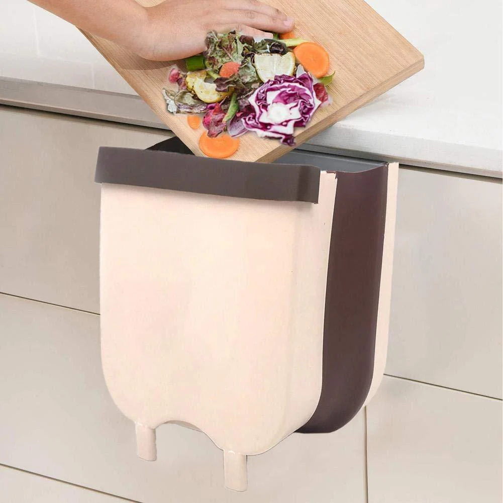 Wall-mounted compost bin with a cutting board full of vegetables above it on a kitchen counter.