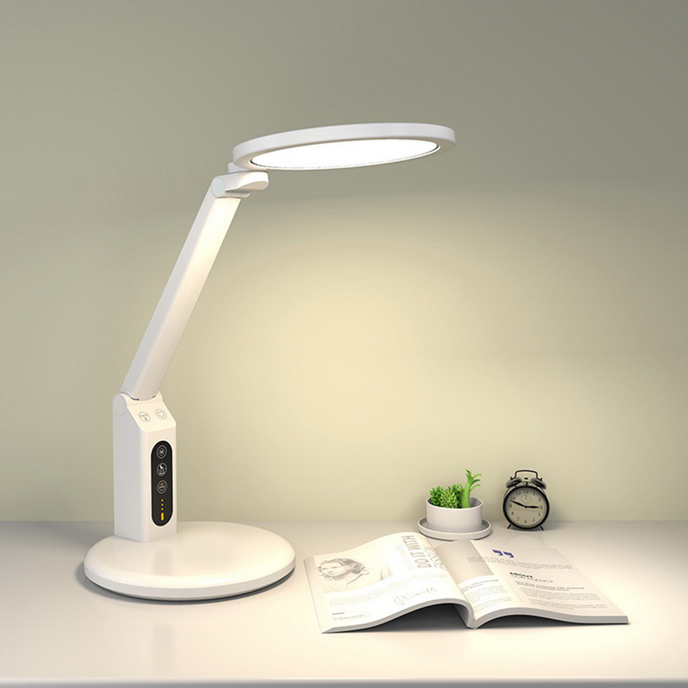 White LED desk lamp on a table with an open book and small plant