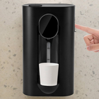 Black wall-mounted coffee machine dispensing a white cup on a textured wall background