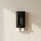 Black wall-mounted device with two white nozzles on a beige wall