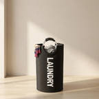 Black laundry basket with 'LAUNDRY' text on a wooden floor.