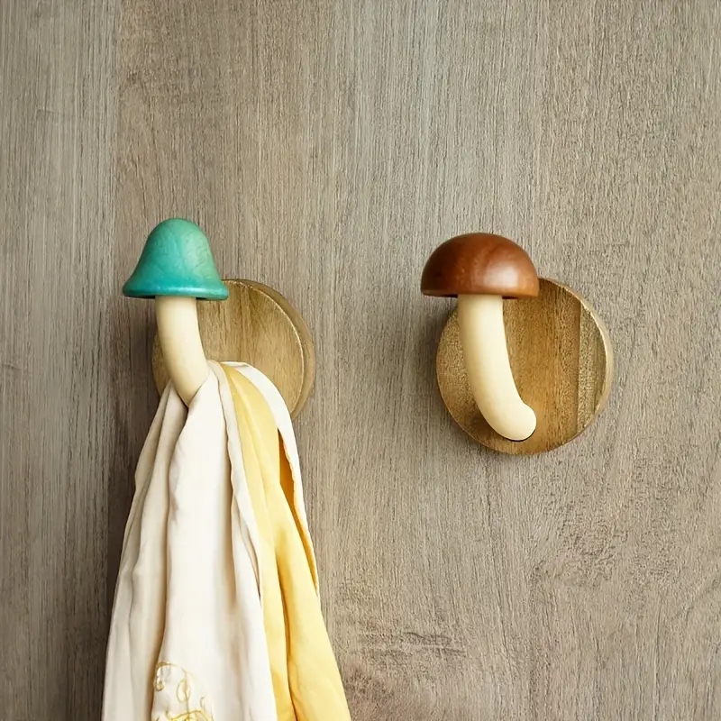 Two mushroom-shaped wall hooks on a wooden wall with a towel hanging from one of them.