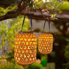 Two woven solar lanterns hanging from a tree branch in a garden setting.