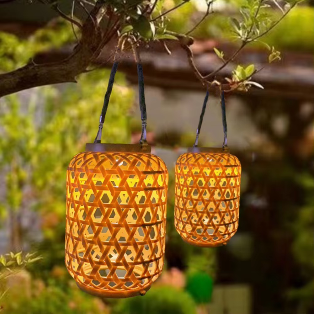 Two woven solar lanterns hanging from a tree branch in a garden setting.