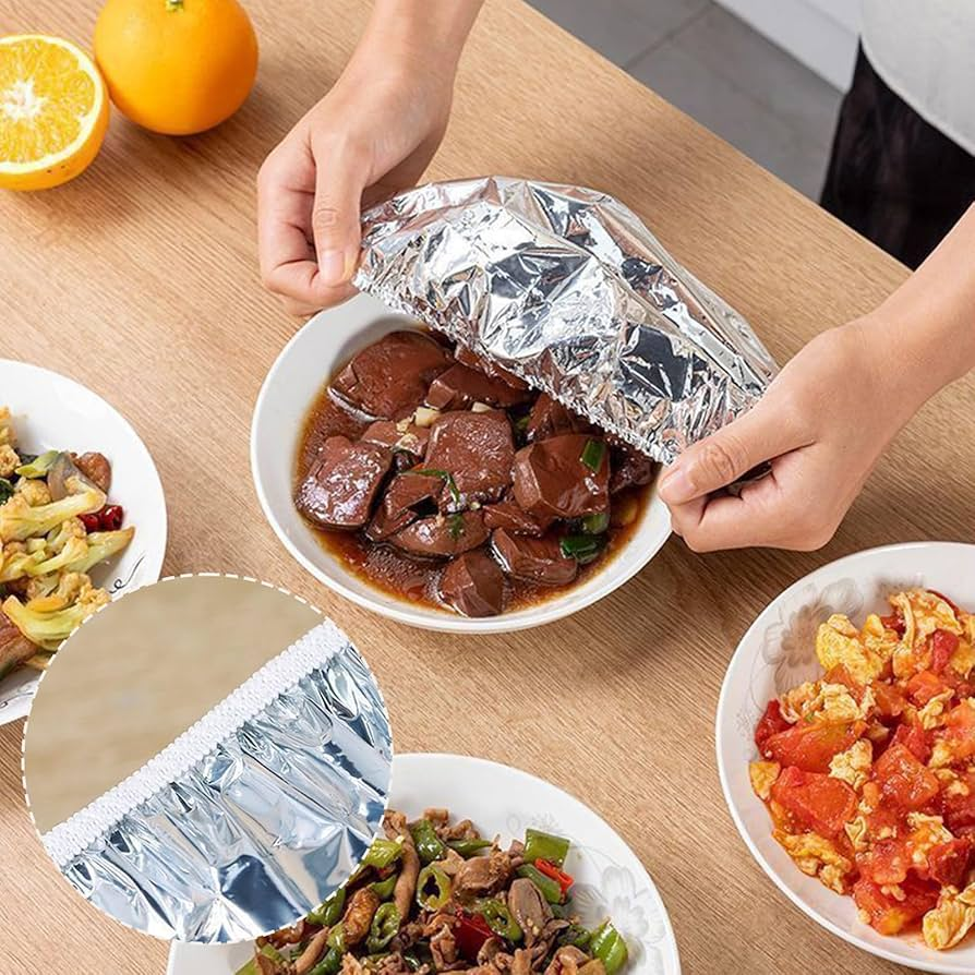 Person opening a foil-wrapped dish on a table with other food items.
