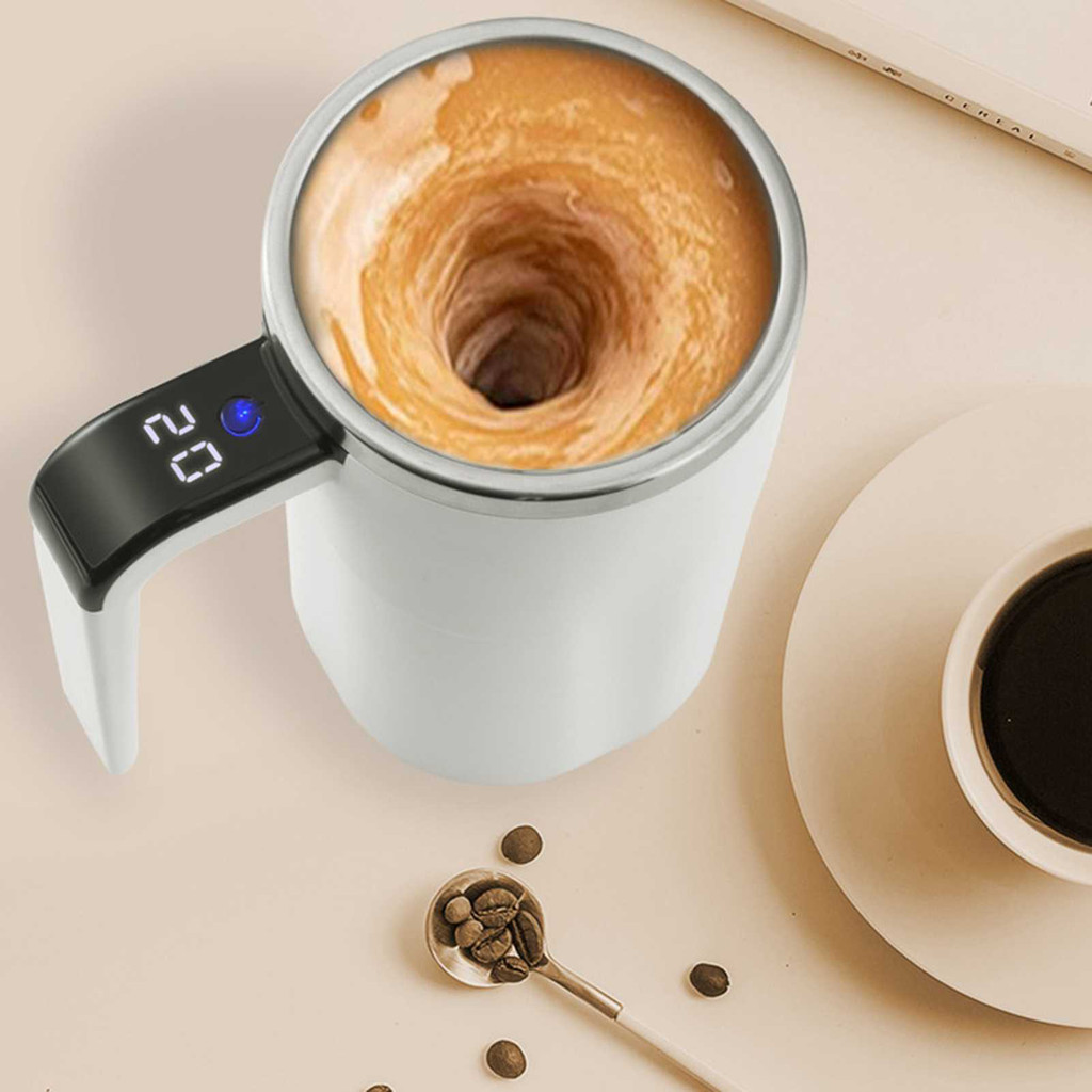 White mug with digital temperature display on a beige surface with coffee beans and another cup.