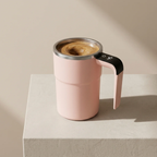 Pink travel mug with a handle filled with coffee on a beige background