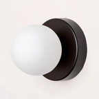Modern wall-mounted light fixture with a matte black circular backplate and a frosted white spherical glass shade, shown against a plain off-white background.