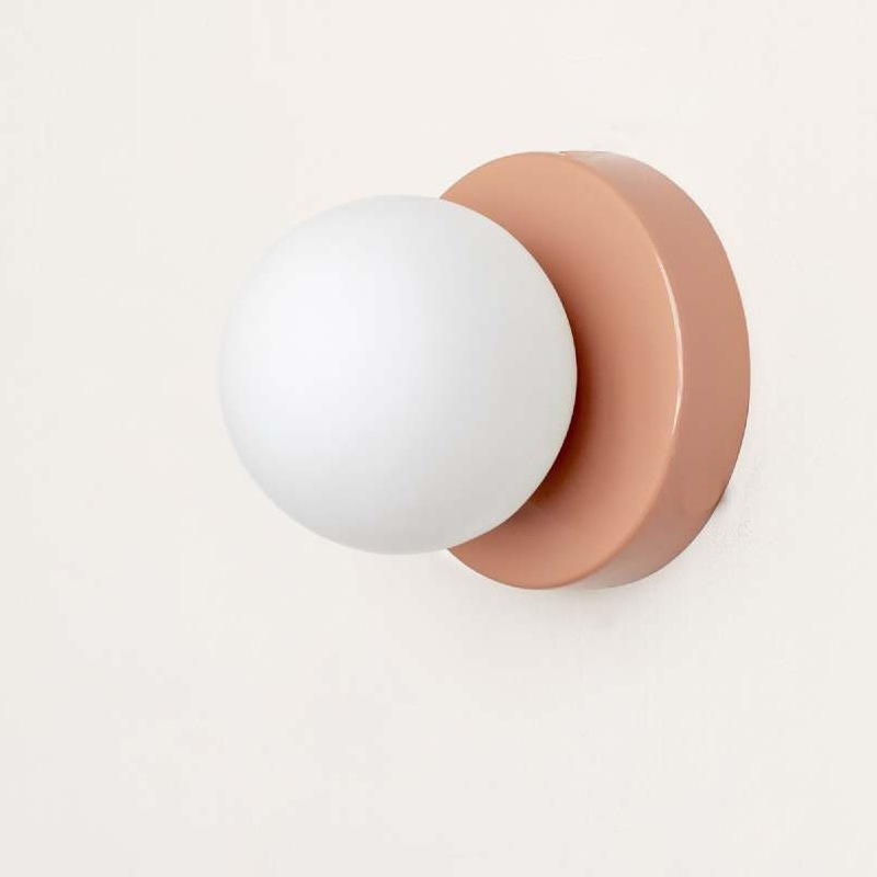 Wall sconce with white globe light and rose gold finish on a light gray background