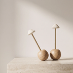 Two mushroom-shaped table lamps with light wood bases and white conical shades, displayed on a stone surface against a warm beige wall.