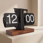 A black flip clock with large white numerals and a rectangular wooden base, photographed on a light beige pedestal in a clean interior setting.