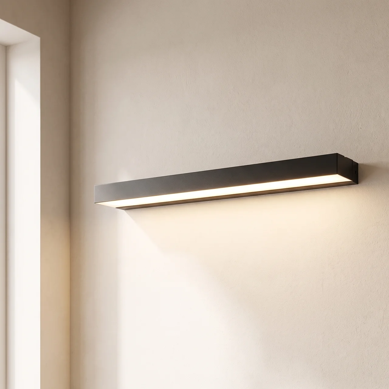 A modern rectangular wall sconce light fixture in a matte black finish, mounted on a textured beige wall and casting a warm glow downward.