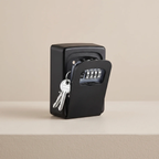 A black key safe with a four-digit combination lock and attached keys, shown open on a beige surface against a matching beige background.