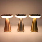Three modern table lamps with brushed metal cone-shaped bases and glowing white circular light bands, shown in copper, silver, and gold finishes against a warm beige background.