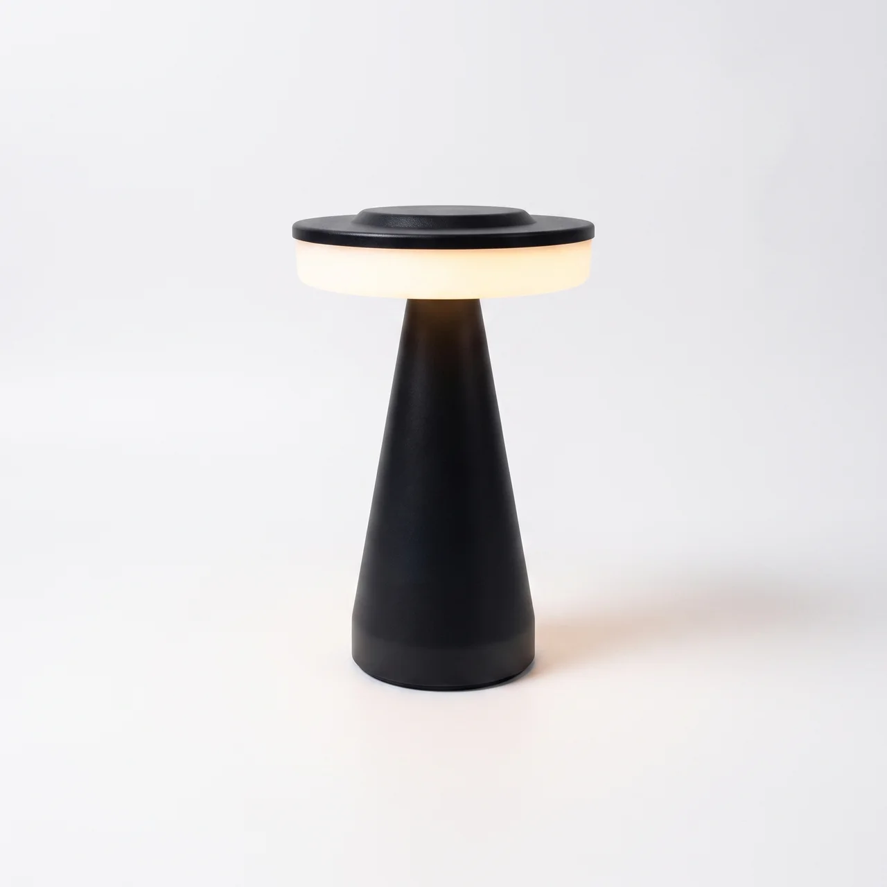 A modern black table lamp with a tapered base and a circular light-emitting top, shown on a clean white background.
