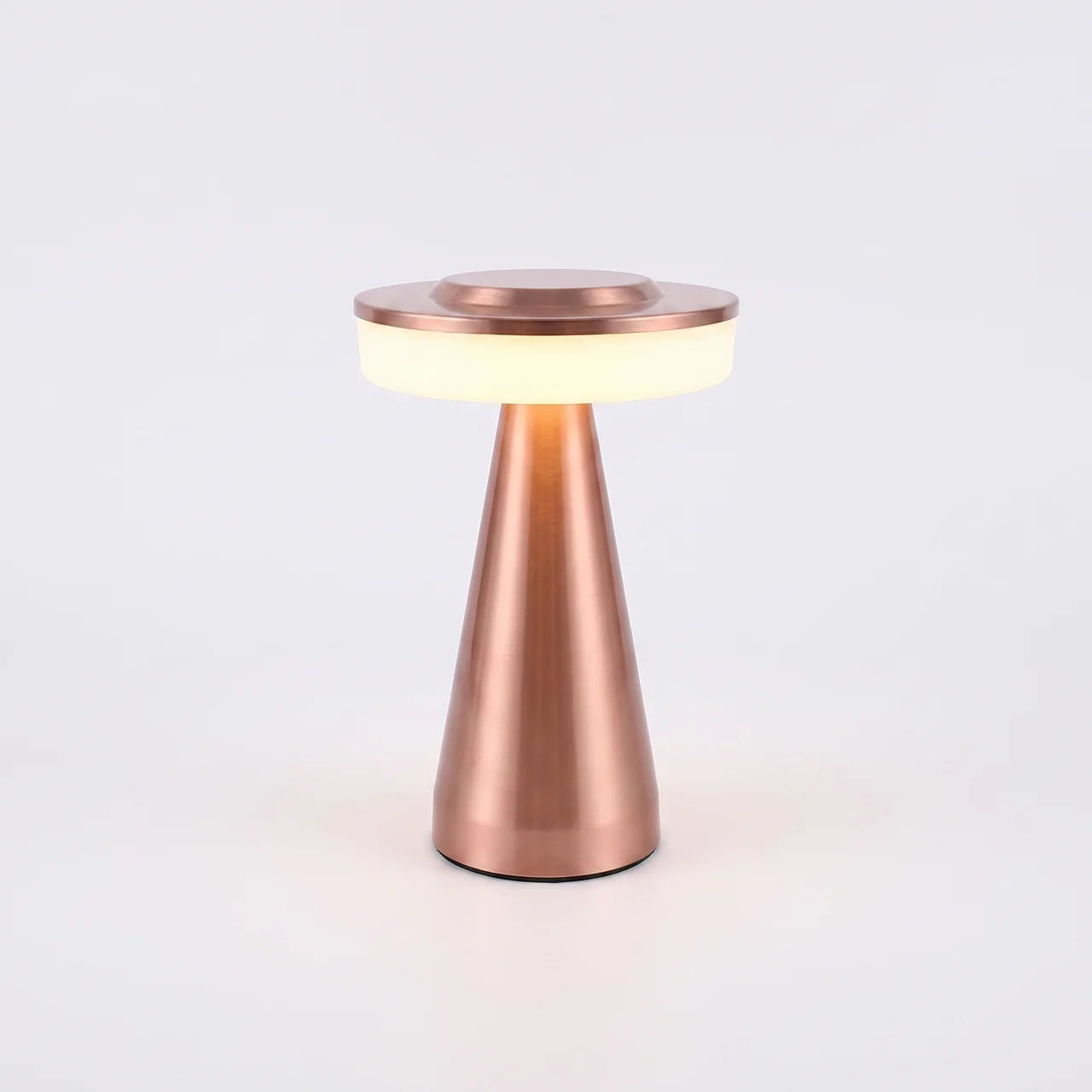 A modern table lamp with a tapered metallic rose gold base and a circular glowing white diffuser on top, set against a clean white background.