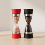 Two hourglass-style salt and pepper mills standing side by side on a light wood surface against a warm beige background. The left mill has a red top and base with silver metal bands and is filled with pink salt.
