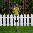 Solar-powered artificial lavender garden stake with glowing warm white lights, set in green grass in front of a white picket fence and wooden trellis.
