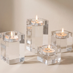 Four clear acrylic cube candle holders, each containing a lit tealight candle, arranged on a warm beige surface against a matching beige background.