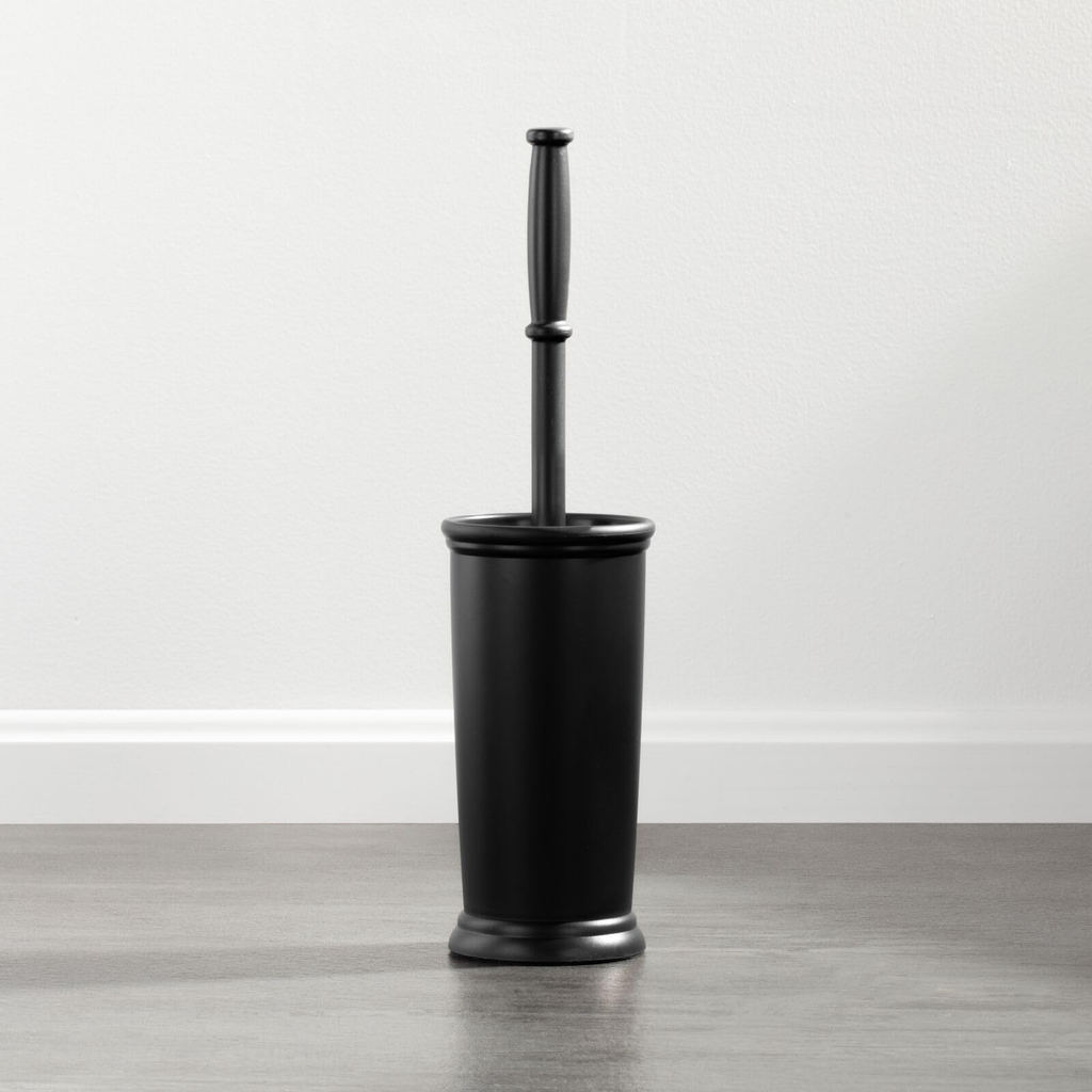 Black toilet brush with holder on a wooden floor against a white wall
