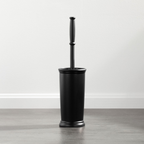 Black toilet brush with holder on a wooden floor against a white wall