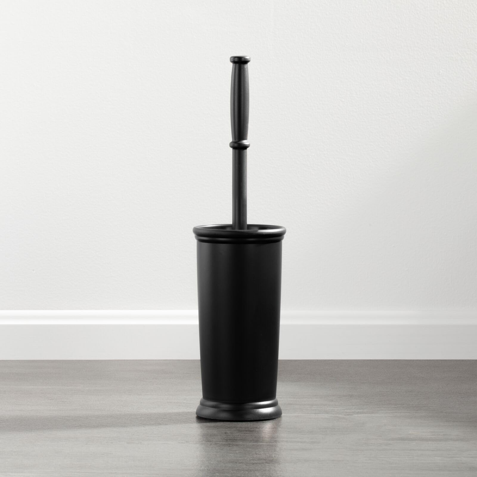 Black toilet brush with holder on a wooden floor against a white wall