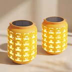 Two yellow solar-powered lanterns with a floral cutout pattern, glowing with warm light, set against a neutral beige background with soft shadows.