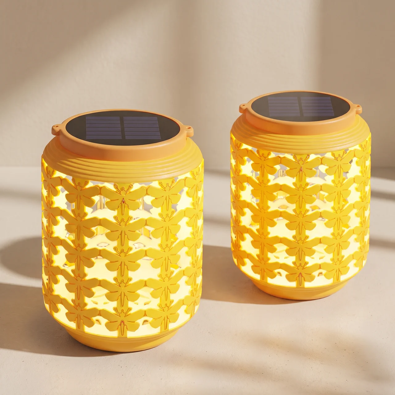 Two yellow solar-powered lanterns with a floral cutout pattern, glowing with warm light, set against a neutral beige background with soft shadows.