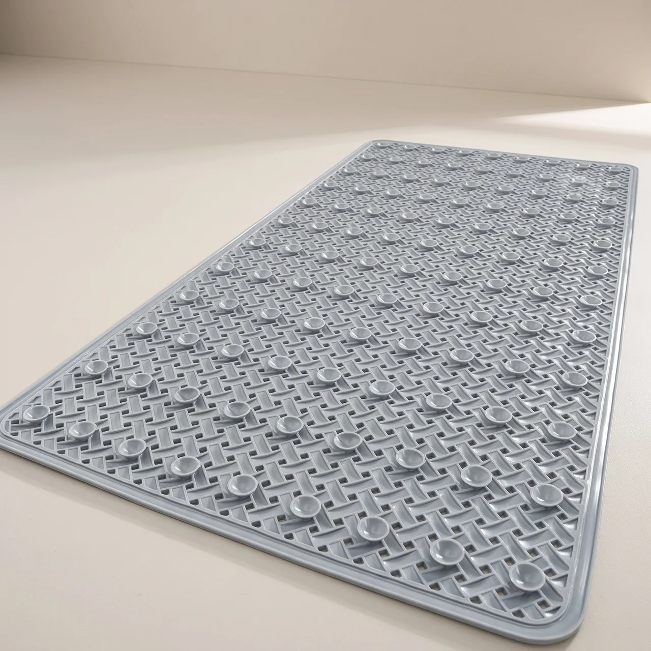 A gray textured rectangular mat with raised circular nubs and a raised border, photographed on a plain light beige surface.