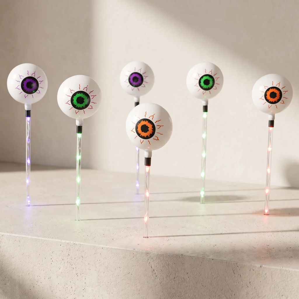Five novelty goggle-style lawn lights with white spherical lenses and multicolor glowing eyes, arranged on a light stone surface against a beige wall.