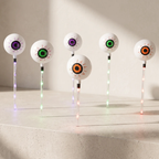 Five novelty goggle-style lawn lights with white spherical lenses and multicolor glowing eyes, arranged on a light stone surface against a beige wall.