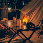 Camping scene with a tent, table, candles, and fire pit at night.