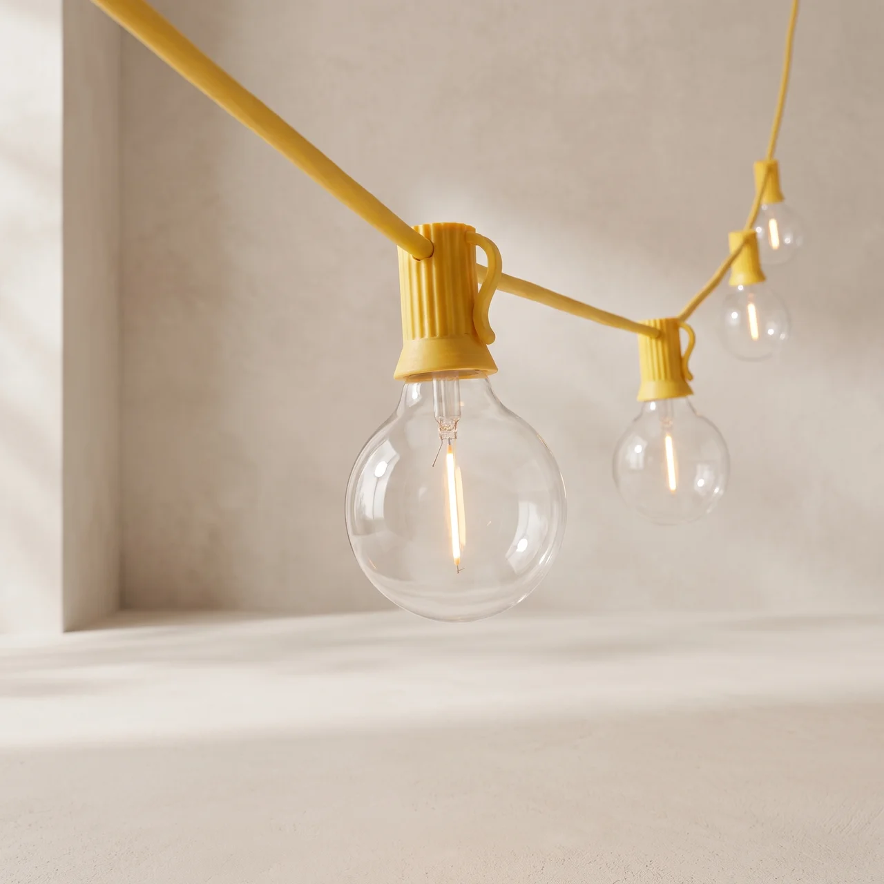 Yellow string light bulbs with clear glass globes hanging against a warm beige wall and floor.