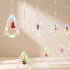 Hanging Christmas tree-shaped string lights with small LED fairy lights and miniature Santa Claus and tree ornaments inside clear plastic frames, set against a warm beige wall.