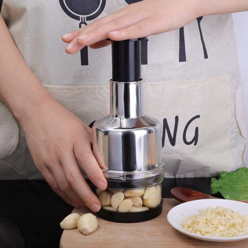 Person using a garlic press on a wooden cutting board with garlic cloves and a plate of minced garlic.