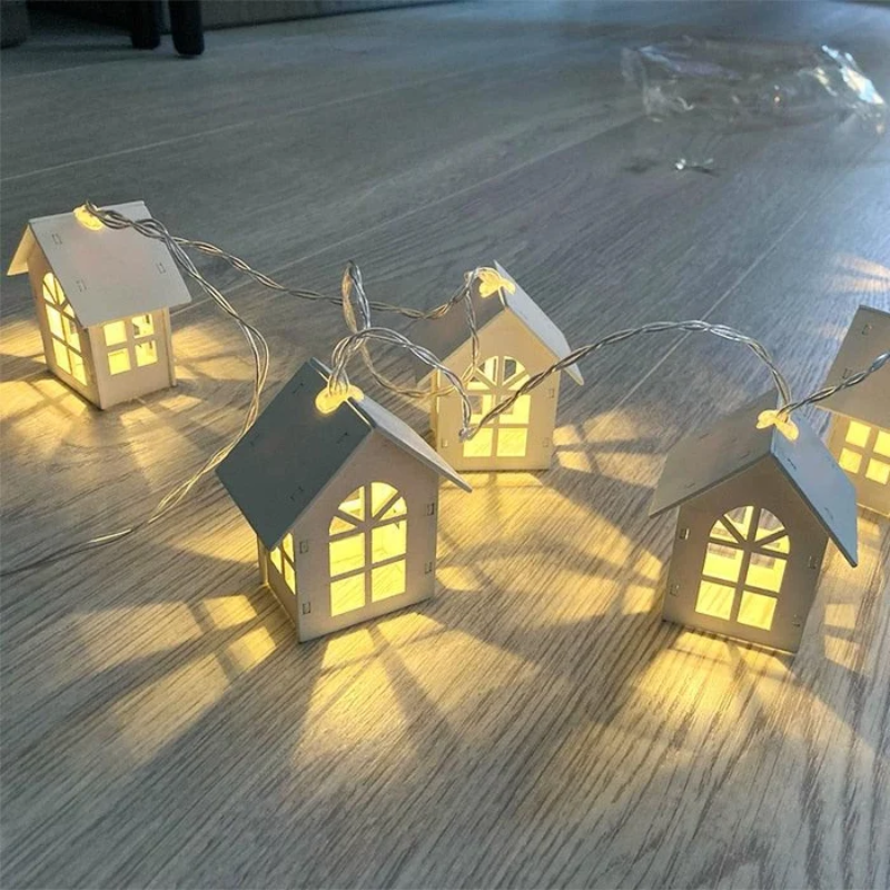 A string of miniature house-shaped fairy lights with warm yellow glowing windows, laid out on a light-colored wooden floor.