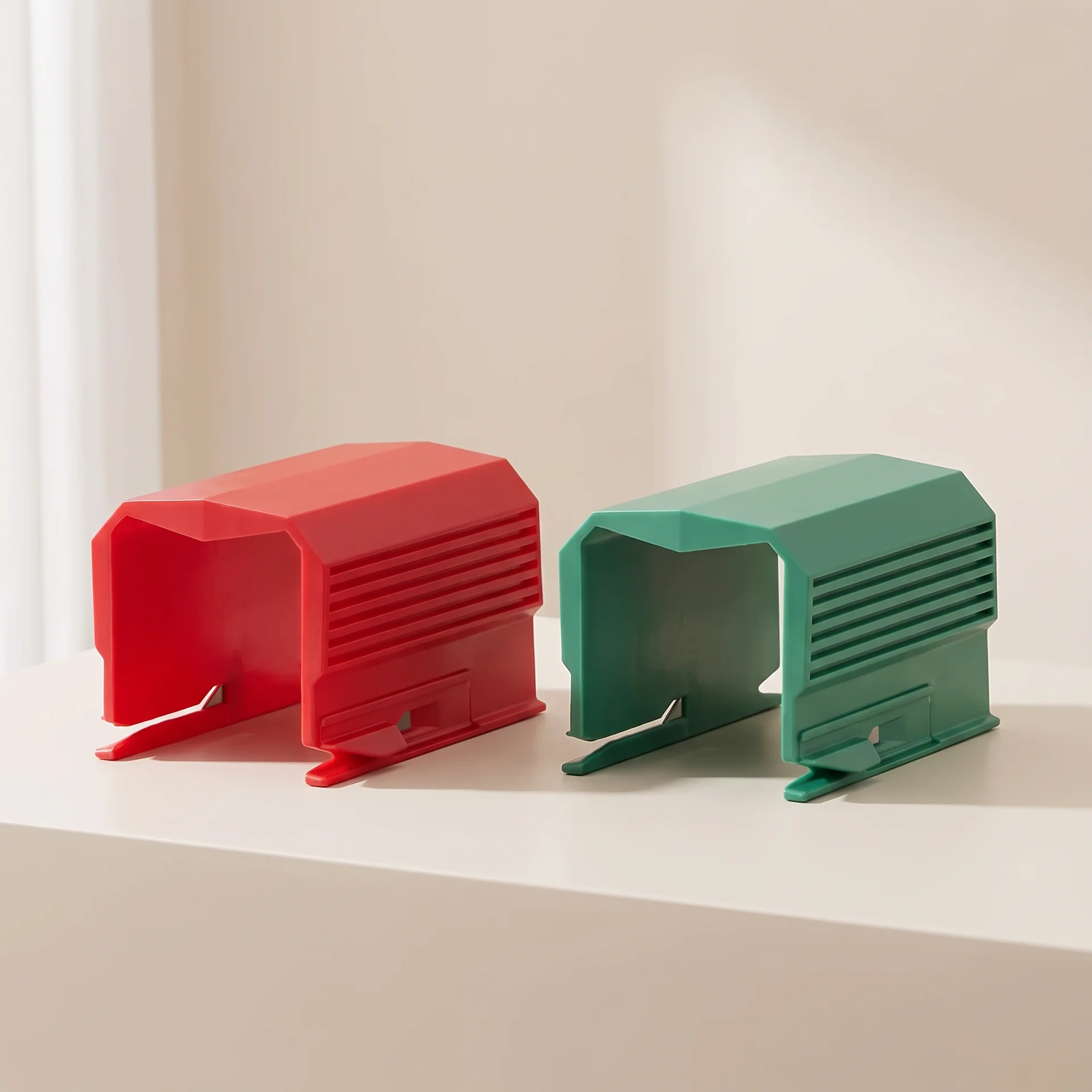 Two small plastic accessory pieces, one red and one green, displayed side by side on a white surface against a warm off-white background.