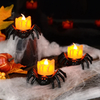 Three Halloween spider-shaped candle holders with glowing orange candles, styled on a dark surface with white faux cobwebbing, autumn leaves, and pumpkins.
