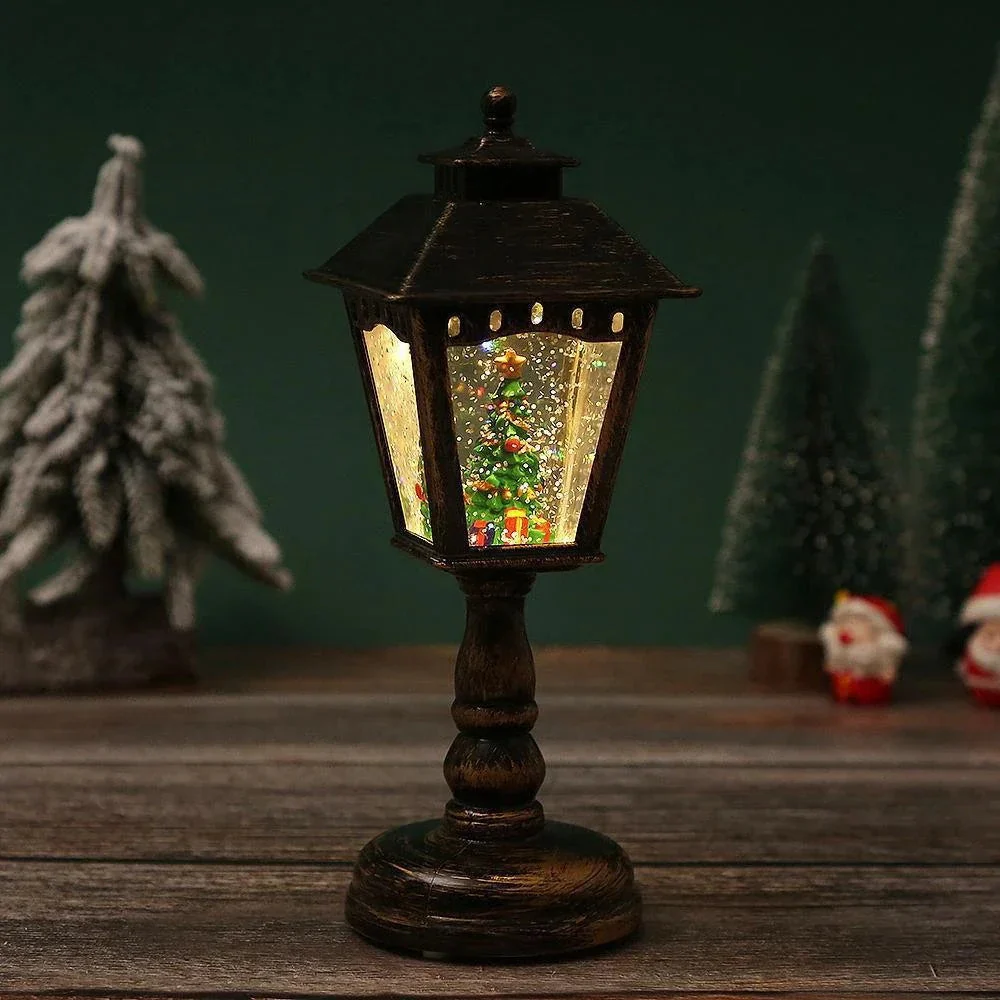 Decorative lamp with a Christmas scene inside, surrounded by small trees and Santa figures on a wooden surface.