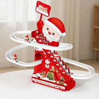 A festive Christmas-themed toy track set featuring a red staircase tower, white spiral tracks, small rolling Santa figures, and a Santa-decorated base, photographed indoors on a tabletop with a softly blurred room background.
