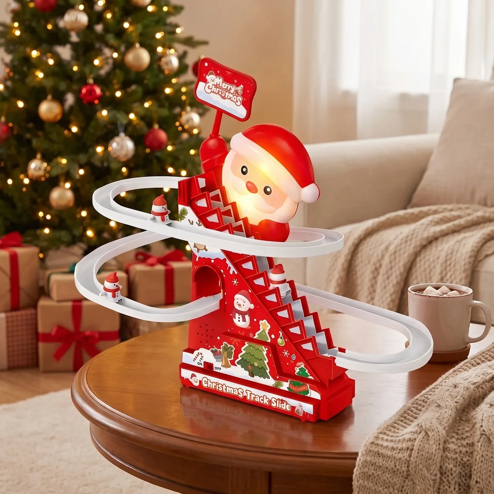 A festive Christmas-themed toy track set on a wooden table in a cozy living room. The red and white toy features a Santa Claus figure, winding white tracks, small decorative hills, and a sign that reads 'Merry Christmas.