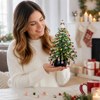 A woman in a white ribbed sweater holds a small decorated Christmas tree ornament in a cozy living room setting with stockings, gifts, and candles in the background.
